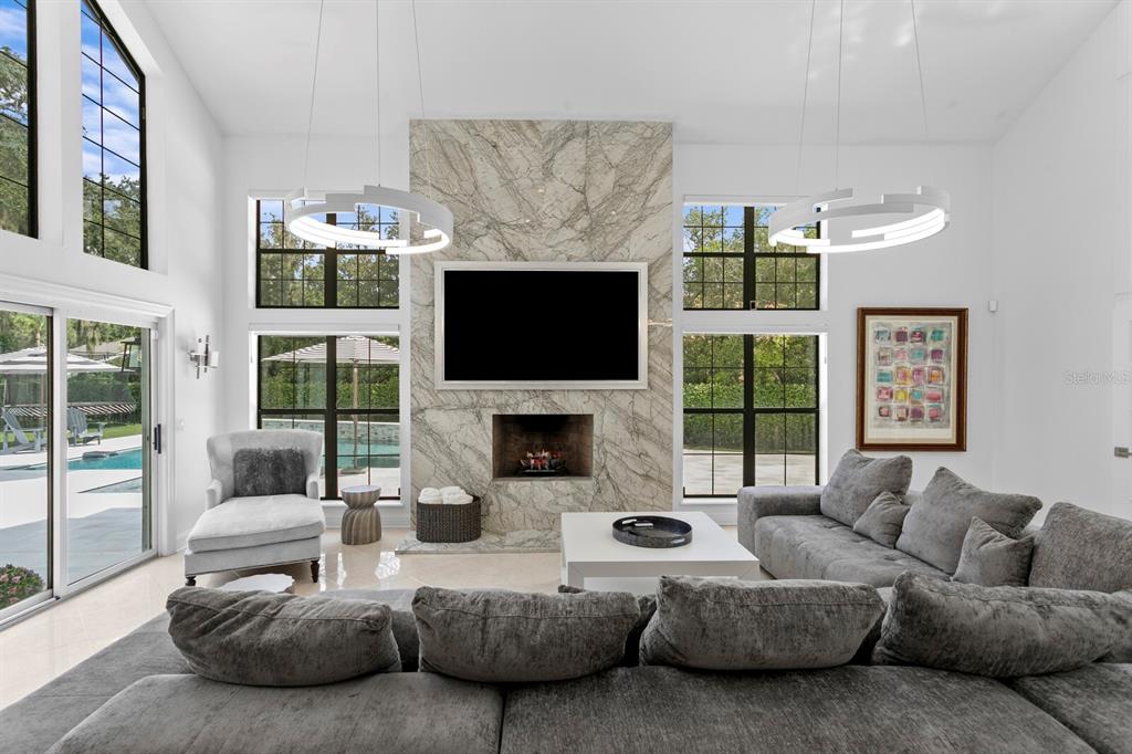 A living room with a stone fireplace, large windows, and a gray sectional sofa — 1001 BAJADA DE AVILA, TAMPA, FL