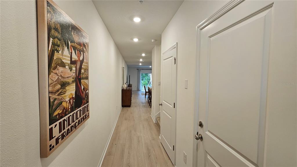 A long hallway with light wood-look flooring leads toward a bright room with a sliding door — 19912 MADERA CIRCLE, VENICE, FL