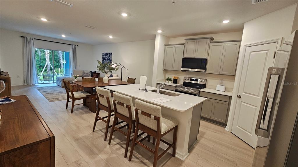 A kitchen with a white island and gray cabinets opens into a dining and living area — 19912 MADERA CIRCLE, VENICE, FL