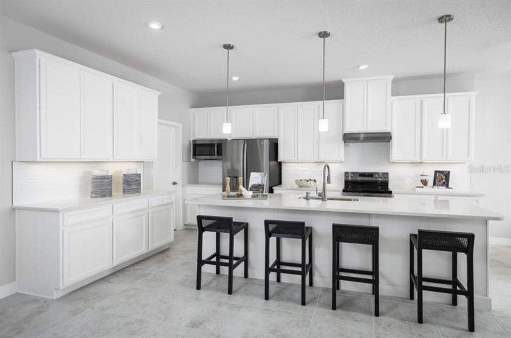 A modern white kitchen features a large island with four black stools and stainless appliances — 8458 SWAN VIEW CIRCLE, LEESBURG, FL