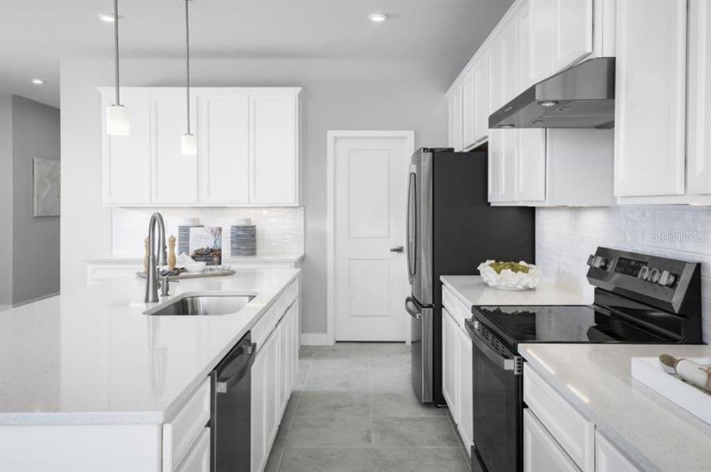 A modern kitchen features white cabinets, quartz countertops, stainless steel appliances, and a central island — 8458 SWAN VIEW CIRCLE, LEESBURG, FL
