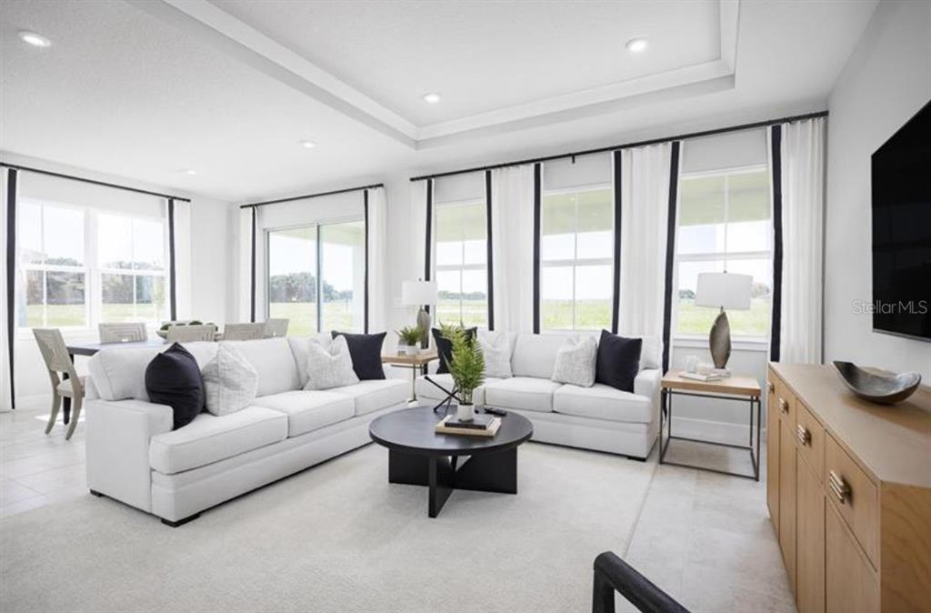 A bright living room features white sofas, a round coffee table, and large windows — 8458 SWAN VIEW CIRCLE, LEESBURG, FL