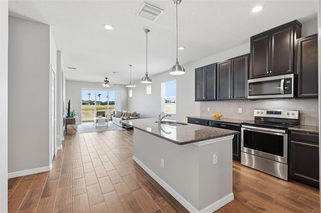 A kitchen with dark cabinets and a granite island opens to a living area — 11908 GREENCHOP PLACE, RIVERVIEW, FL