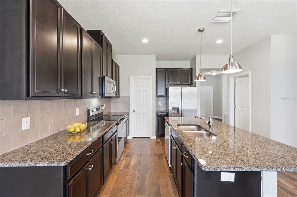 A kitchen features dark wood cabinets, granite countertops, stainless steel appliances, and wood-look tile flooring — 11908 GREENCHOP PLACE, RIVERVIEW, FL
