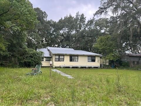 A single-story yellow house with a metal roof sits on a grassy lot with trees — 5040 SE 3RD LANE, TRENTON, FL