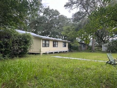 A yellow single-story house with a pier foundation sits on a grassy lot with trees — 5040 SE 3RD LANE, TRENTON, FL