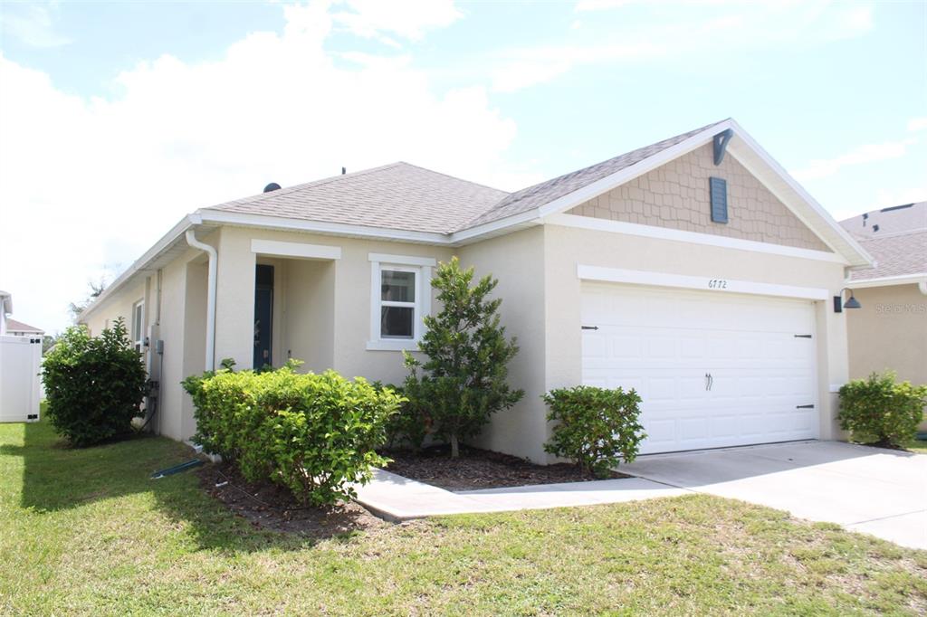 A single-story house with a beige stucco exterior, a two-car garage, and landscaped front yard — 6772 HUNTLEIGH HAMMOCK RD, HARMONY, FL