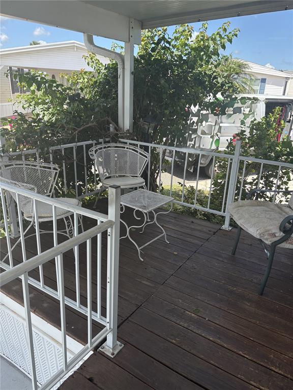 A wooden deck features white metal patio furniture and railings surrounded by green bushes — 9000 US HIGHWAY 192 UNIT 565, CLERMONT, FL