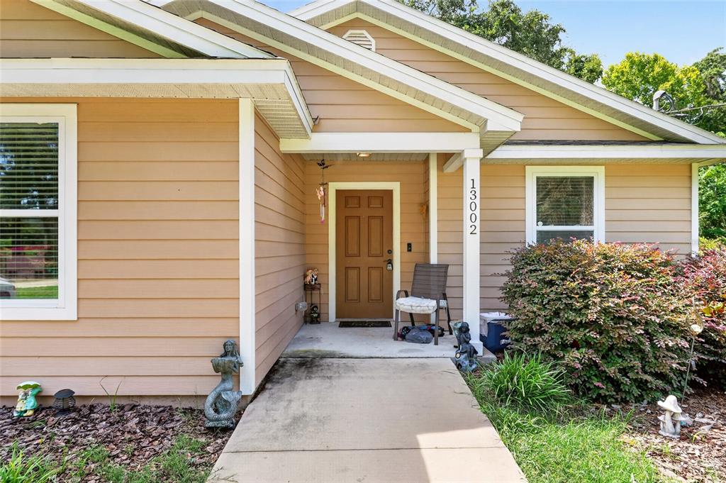 The exterior of a tan house features a brown front door and a concrete walkway — 13002 SW 174TH STREET, ARCHER, FL