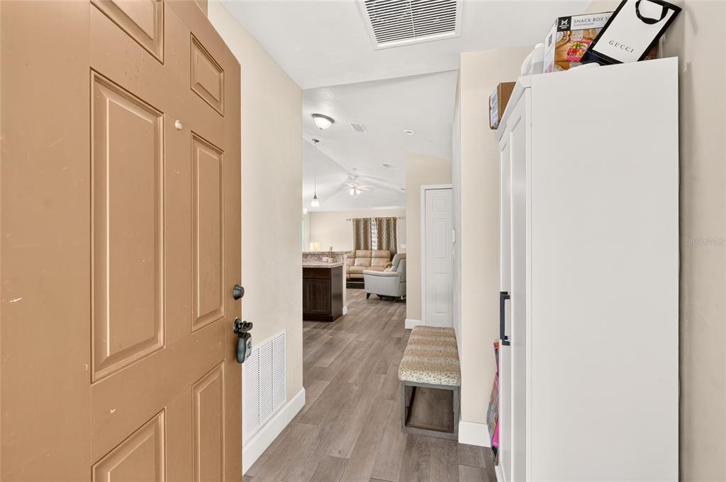 An entryway features a brown door, wood-look flooring, a white storage cabinet, and a bench — 13002 SW 174TH STREET, ARCHER, FL
