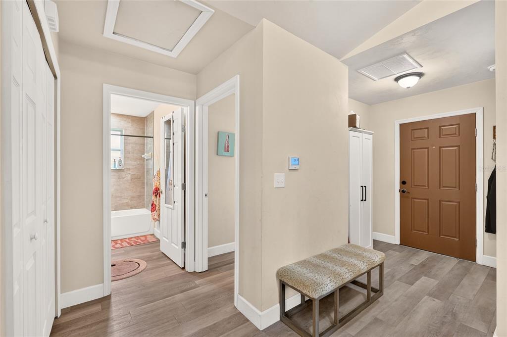 An entryway with wood-look flooring, a brown front door, a bench, and a bathroom view — 13002 SW 174TH STREET, ARCHER, FL