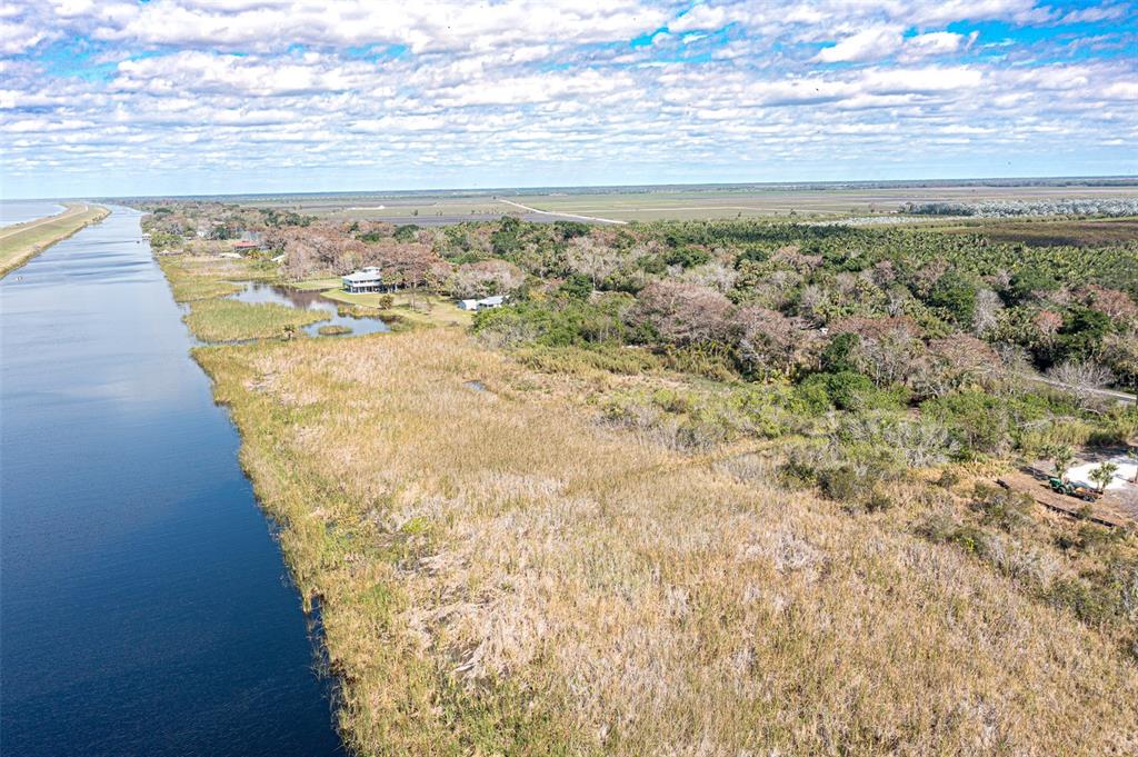 An aerial view shows a canal bordering a grassy marshland and a wooded residential area — 15460 SW CONNERS HIGHWAY, OKEECHOBEE, FL