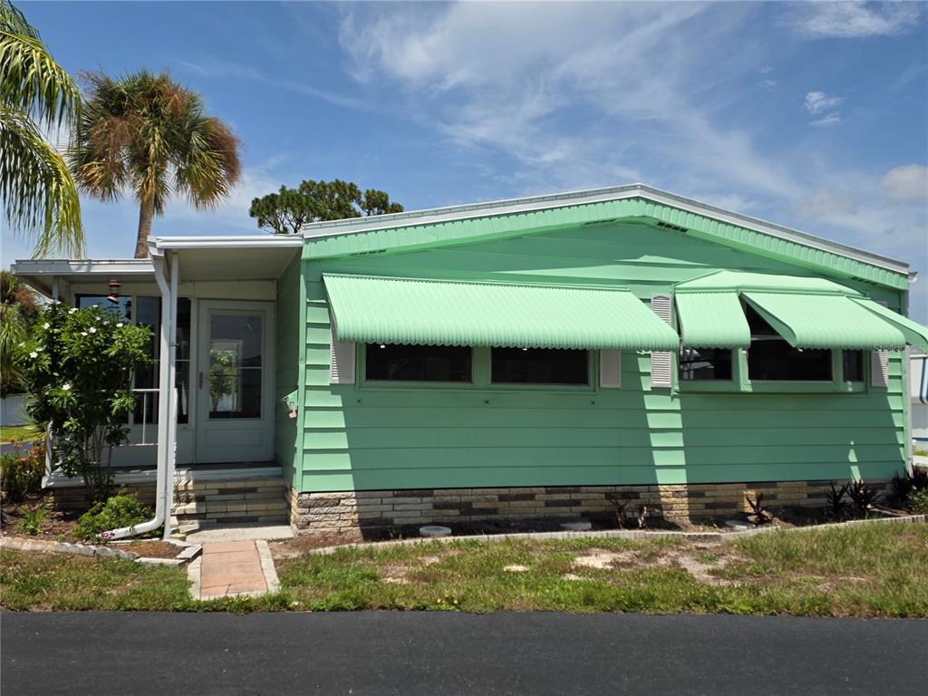A light green mobile home features metal awnings, a small front porch, and brick skirting — 1800 ENGLEWOOD ROAD UNIT 146, ENGLEWOOD, FL