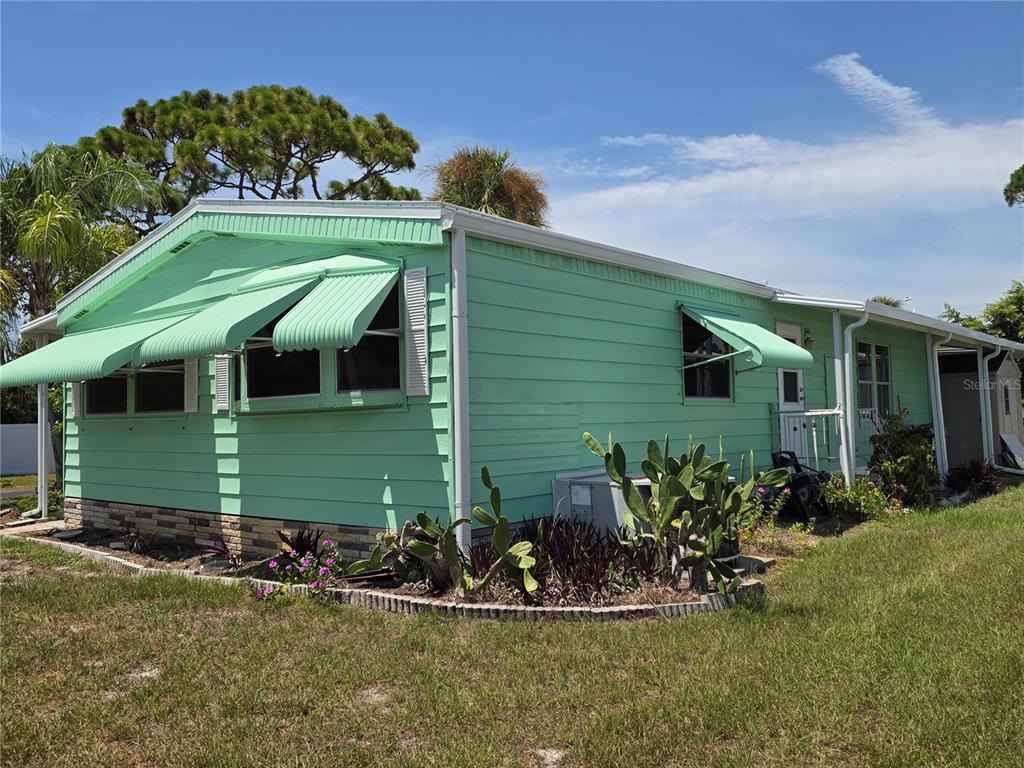 A light green mobile home features metal window awnings and a small garden bed — 1800 ENGLEWOOD ROAD UNIT 146, ENGLEWOOD, FL