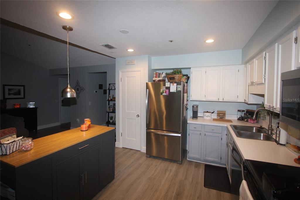 A kitchen features a dark island with a wood countertop, stainless steel appliances, and white cabinetry — 810 LOCH CALDER UNIT 25, APOPKA, FL