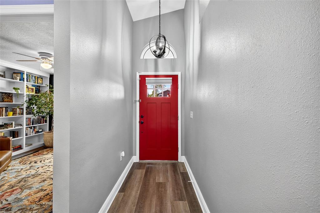 An entryway features a bright red front door, wood-look flooring, and a modern pendant light — 1721 SPLIT FORK DRIVE, OLDSMAR, FL