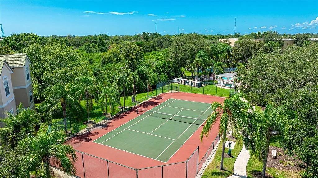 An aerial view shows a fenced tennis court surrounded by trees and a nearby building — 5110 NORTHRIDGE ROAD UNIT 208, SARASOTA, FL