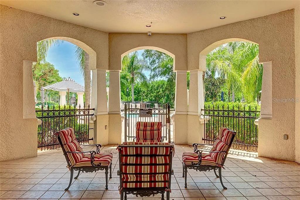 A covered patio features three striped chairs and a metal fence overlooking a pool area — 5110 NORTHRIDGE ROAD UNIT 208, SARASOTA, FL