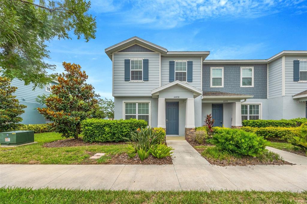 A two-story light blue townhouse with a covered entryway and a small front garden — 14478 PROMENADE, ODESSA, FL