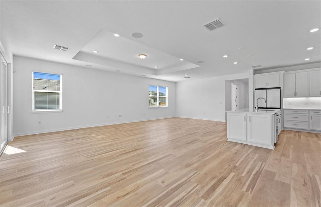 An open-concept living area features light wood flooring, white walls, and an adjacent kitchen — 13816 SUNLIGHT MEADOW DRIVE, RIVERVIEW, FL