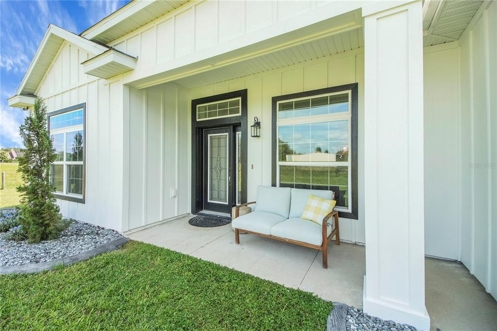 A white farmhouse-style home features a covered front porch with a light blue loveseat — 10757 COUNTY ROAD 223, OXFORD, FL