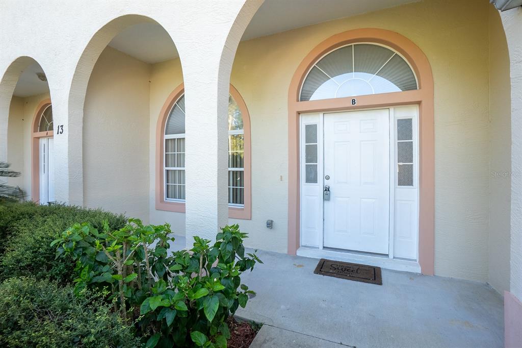 The exterior entrance of a building features arched walkways, white doors, and a small garden — 13 BUTTONWOOD LANE, PALM COAST, FL