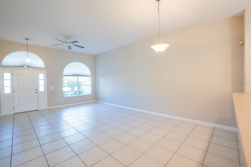 An empty room with light-colored tile flooring, arched windows, a ceiling fan, and pendant lighting — 13 BUTTONWOOD LANE, PALM COAST, FL