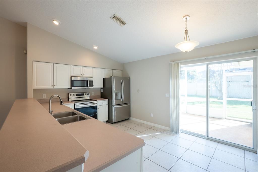 A kitchen with white cabinets, stainless steel appliances, and a breakfast bar overlooks a patio — 13 BUTTONWOOD LANE, PALM COAST, FL