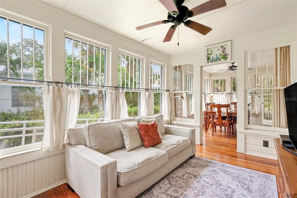 A sunroom with a light-colored sofa, hardwood floors, and large windows overlooking palm trees — 7 MITCHELL STREET, COCOA, FL