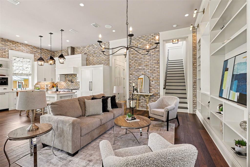 An open-concept living room and kitchen featuring exposed brick walls, hardwood floors, and a staircase — 7 MITCHELL STREET, COCOA, FL