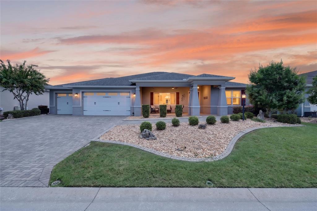 A single-story house with a paved driveway, three-car garage, and landscaped front yard at sunset — 8745 SW 94TH AVENUE, OCALA, FL