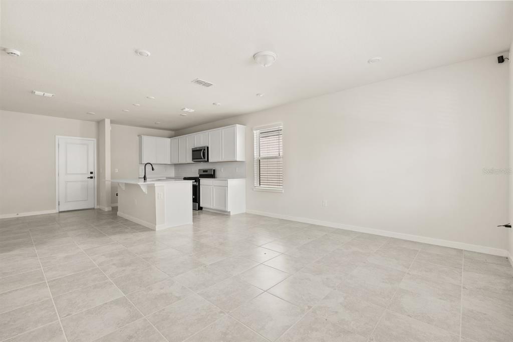 A kitchen with white cabinets and an island opens into a large, tiled living area — 4066 FEATHER TREE DRIVE, APOPKA, FL