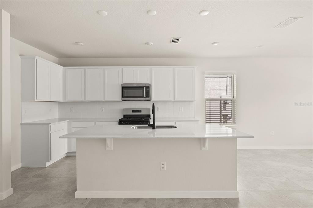 A modern kitchen features white cabinets, a large central island, and stainless steel appliances — 4066 FEATHER TREE DRIVE, APOPKA, FL