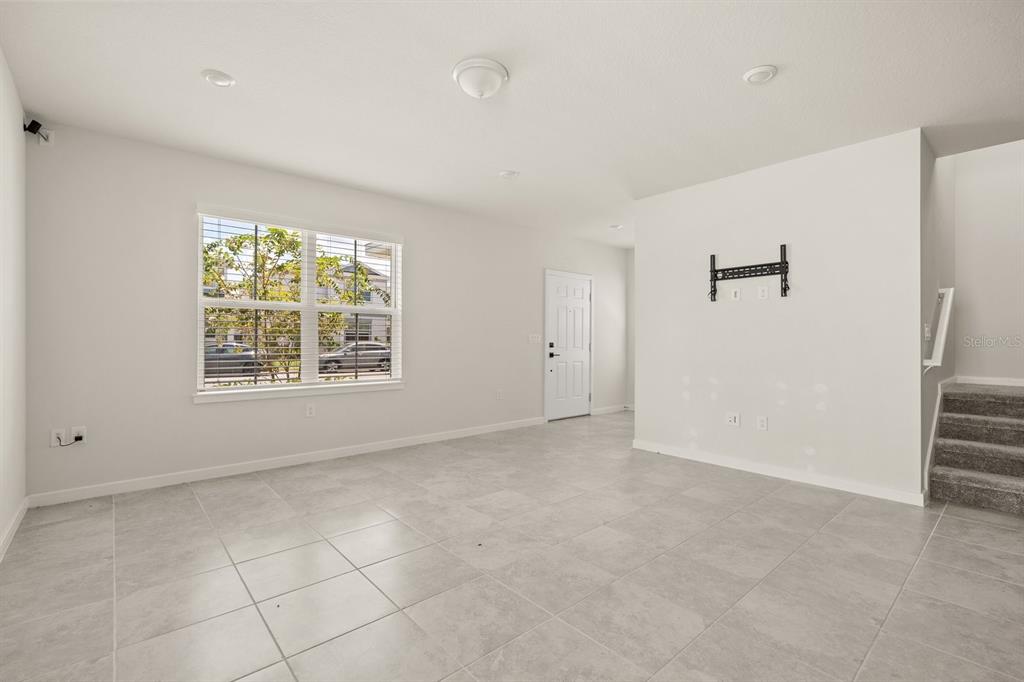A bright living room features light gray tile flooring, white walls, and a wall-mounted television bracket — 4066 FEATHER TREE DRIVE, APOPKA, FL