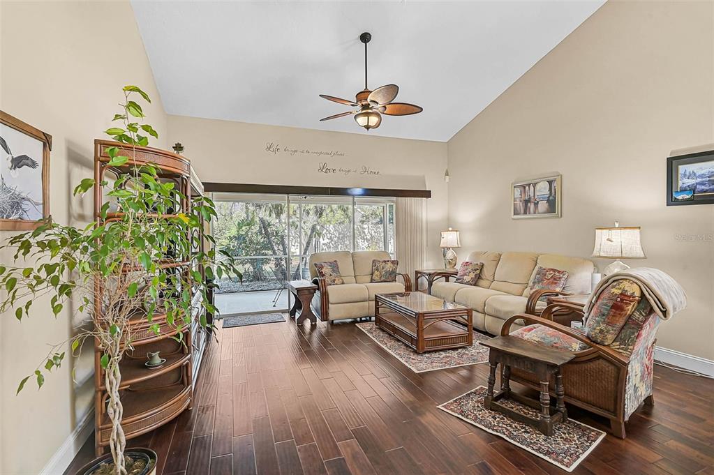 A living room with hardwood floors, a vaulted ceiling, a ceiling fan, and sliding glass doors — 4041 MURFIELD DRIVE E, BRADENTON, FL