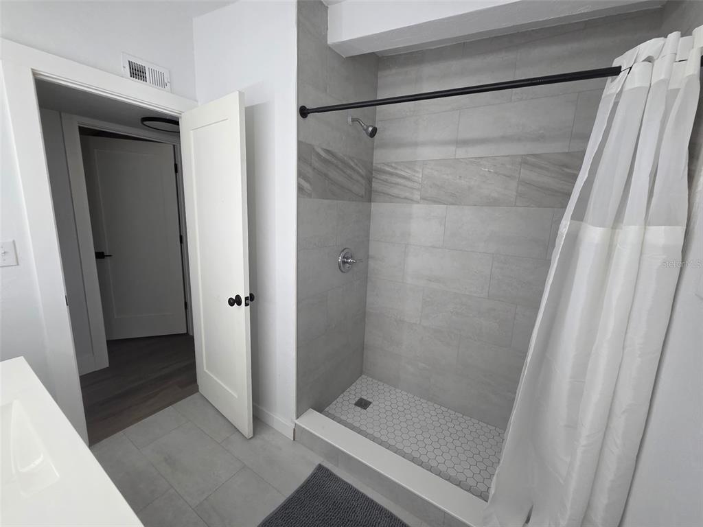 A bathroom features a tiled walk-in shower with a black rod and white curtain — 2839 NE 10TH DRIVE, GAINESVILLE, FL