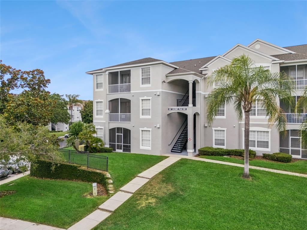 A three-story apartment building with screened balconies and an exterior staircase on a grassy lawn — 8107 COCONUT PALM WAY UNIT 205, KISSIMMEE, FL