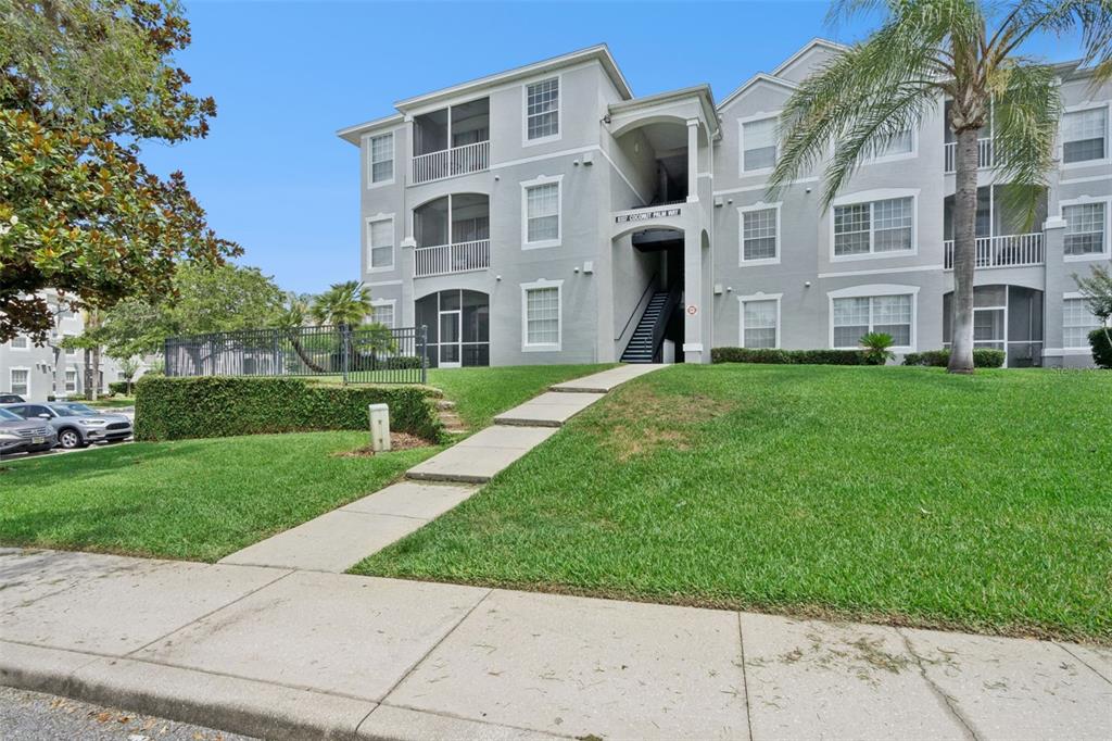 A three-story apartment building with gray siding, screened balconies, and a concrete walkway — 8107 COCONUT PALM WAY UNIT 205, KISSIMMEE, FL
