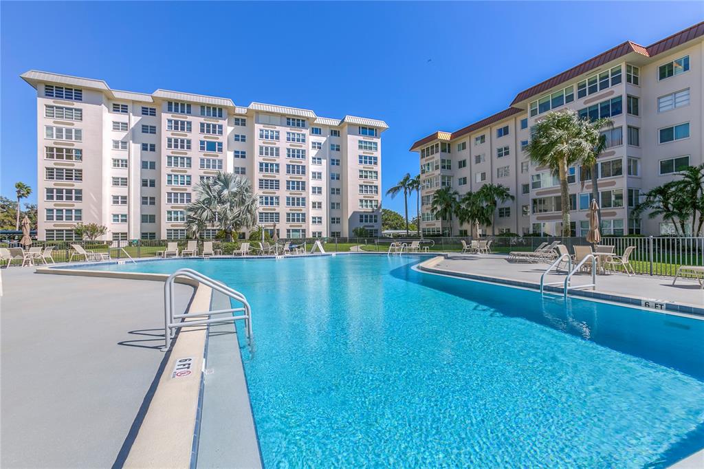 A swimming pool sits in front of two multi-story residential apartment buildings under a clear sky — 632 EDGEWATER DRIVE UNIT 537, DUNEDIN, FL