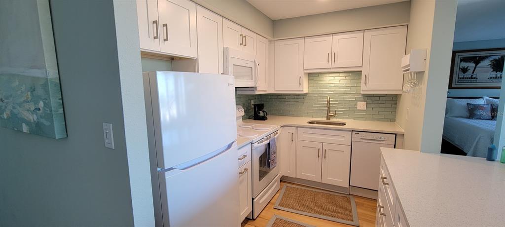 A kitchen features white cabinets, a light blue tile backsplash, and white appliances — 632 EDGEWATER DRIVE UNIT 537, DUNEDIN, FL