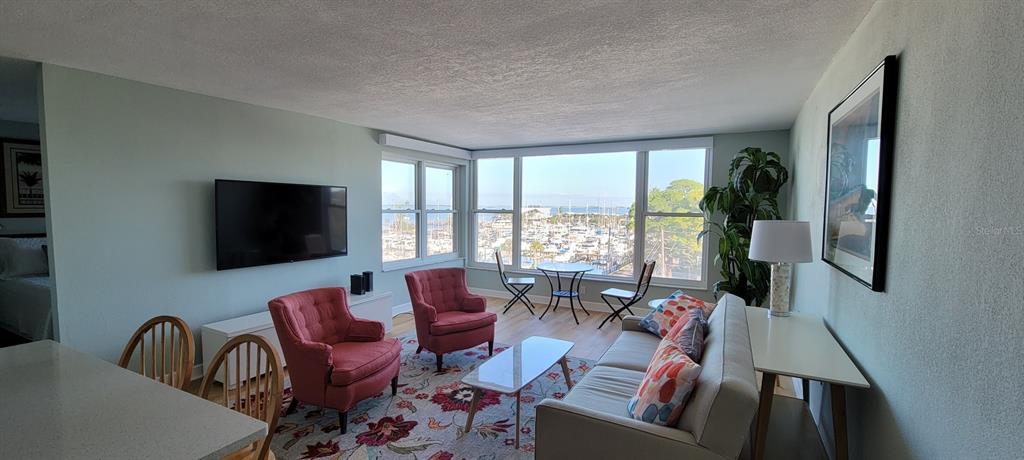 A living room features a sofa, two armchairs, a television, and a view of a marina — 632 EDGEWATER DRIVE UNIT 537, DUNEDIN, FL