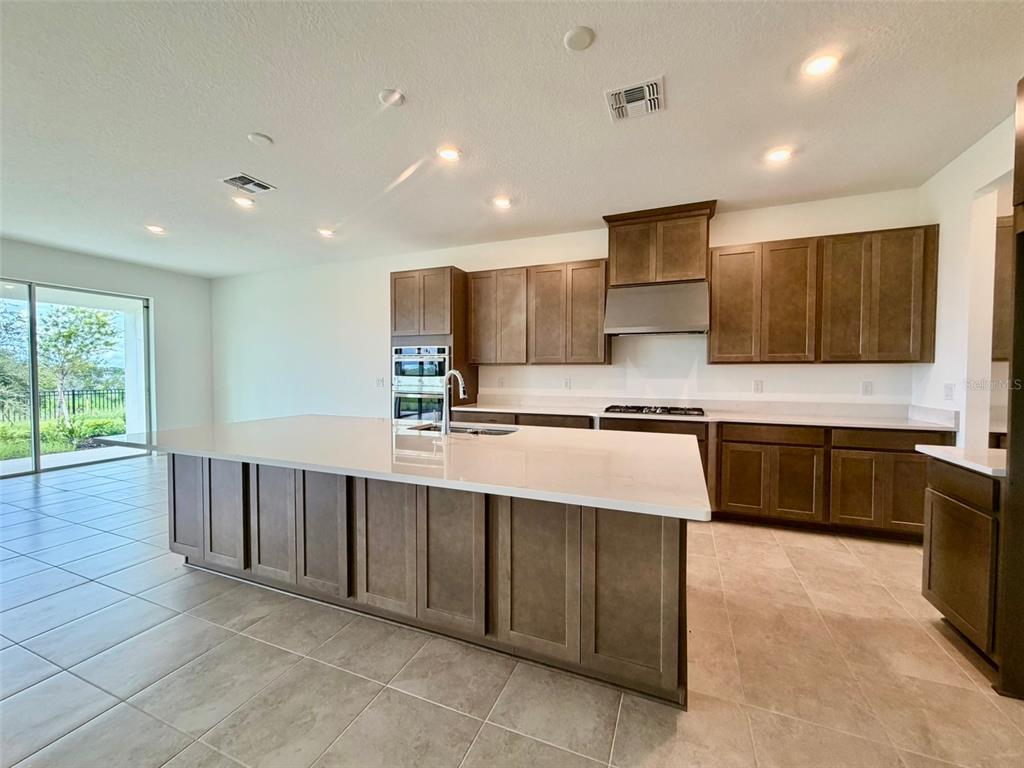 A modern kitchen features dark wood cabinetry, a large white island, and tile flooring — 19350 LOCHSIDE LANE, MOUNT DORA, FL