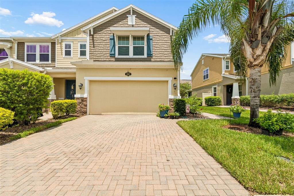 A two-story suburban house with a tan garage, brick paver driveway, and a palm tree — 18907 CORNUTA STREET, LUTZ, FL