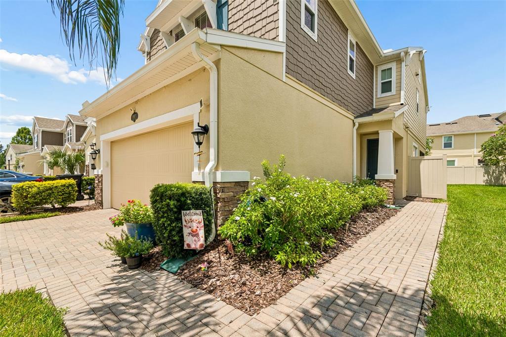 A beige two-story house with a garage, brick paver driveway, and a small front garden — 18907 CORNUTA STREET, LUTZ, FL