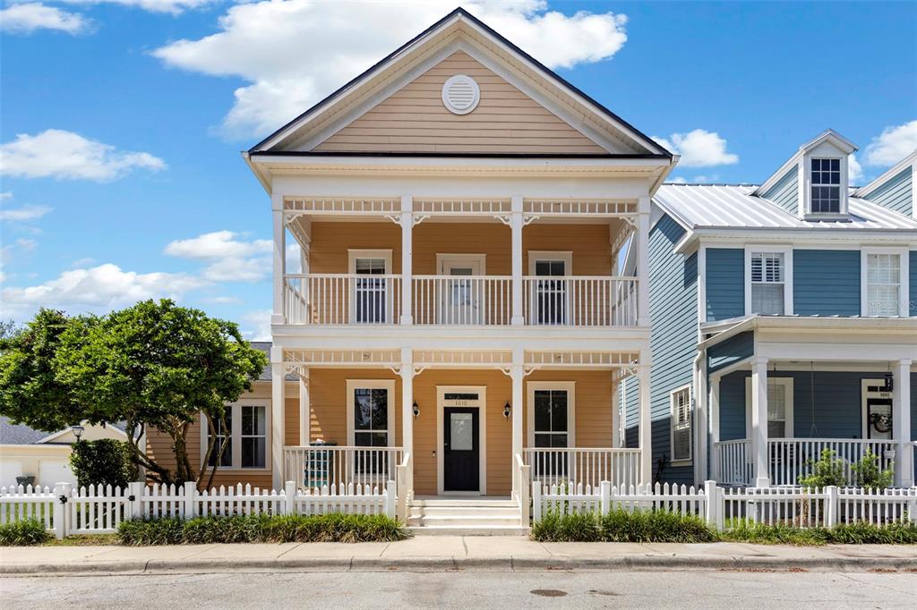 A two-story yellow house with a double-decker front porch and a white picket fence — 1010 PERIWINKLE COURT, CELEBRATION, FL