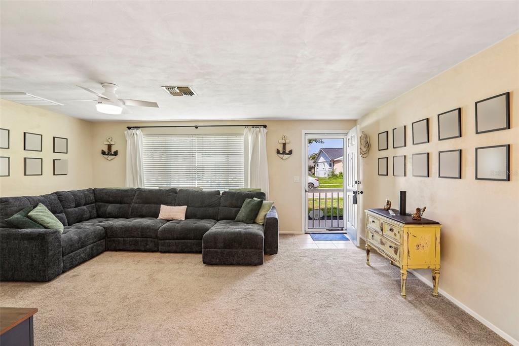 A living room features a large gray sectional sofa, a yellow cabinet, and wall-mounted frames — 3420 PALOMA DRIVE, HOLIDAY, FL
