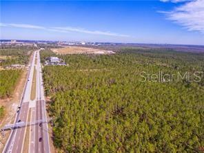 An aerial view shows a multi-lane highway running alongside a large, undeveloped wooded lot — INTERNATIONAL DRIVE, ORLANDO, FL