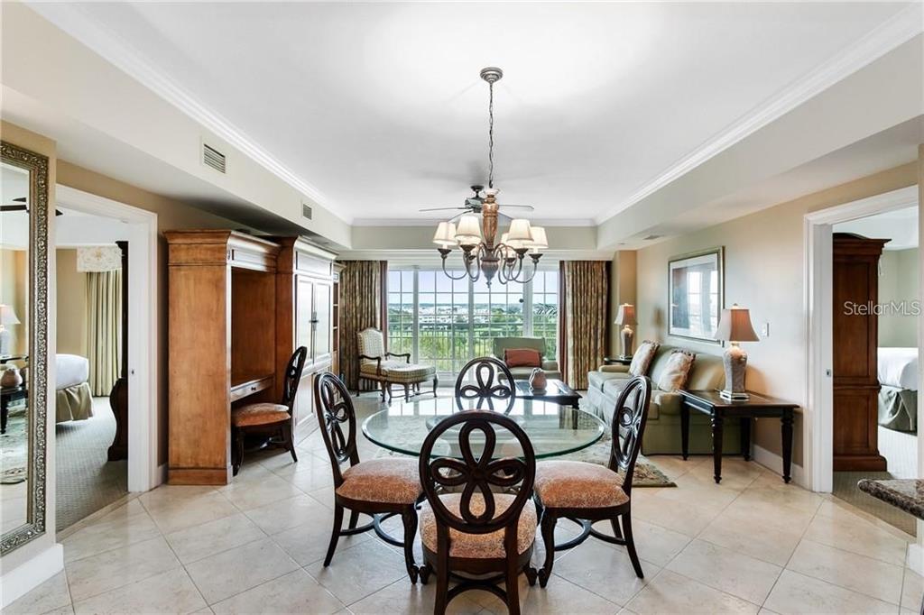 A dining area with a glass table and chandelier opens to a living room with views — 7593 GATHERING DRIVE UNIT 511, REUNION, FL