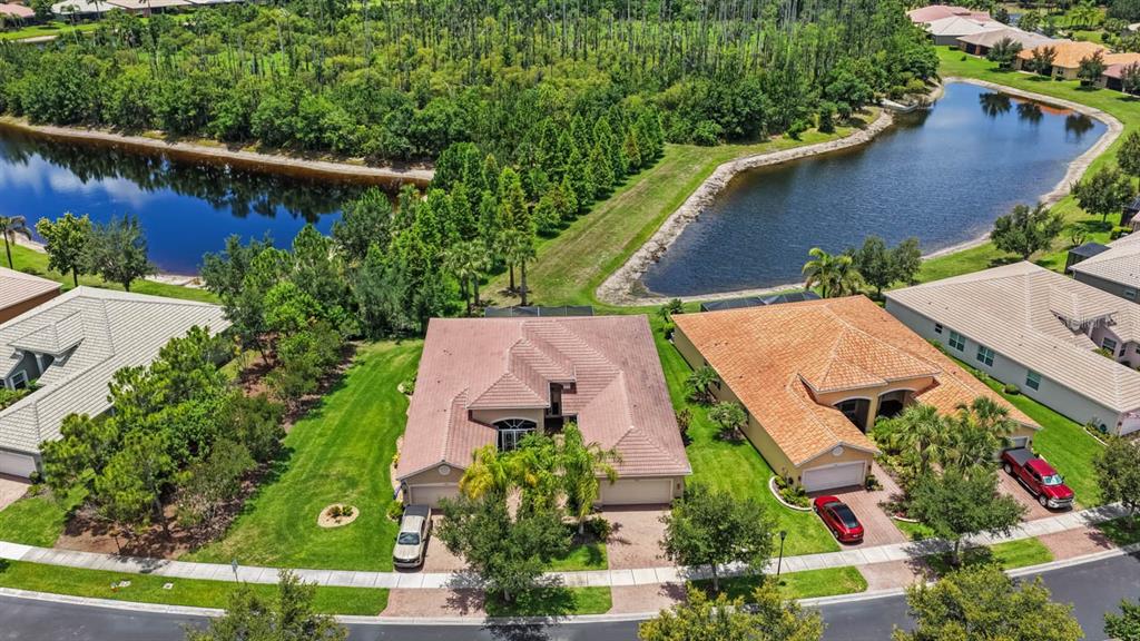 An aerial view shows two suburban houses with tile roofs situated near a large pond — 15665 AURORA LAKE CIRCLE, WIMAUMA, FL