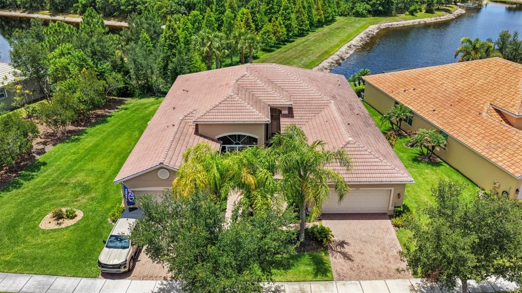 An aerial view of a single-story house with a tiled roof, driveway, and surrounding lawn — 15665 AURORA LAKE CIRCLE, WIMAUMA, FL
